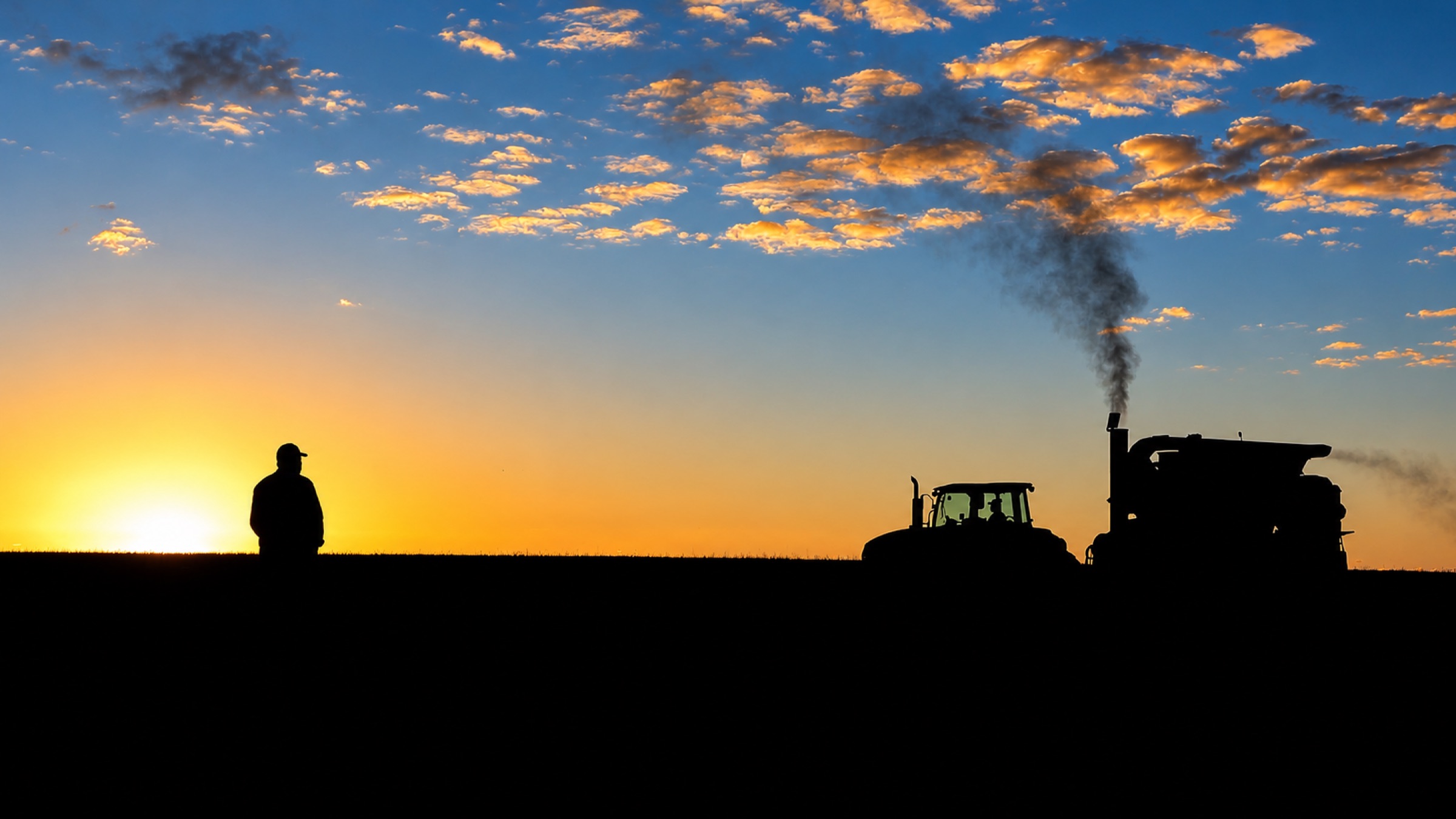 Silueta de un productor junto a una cosechadora al atardecer